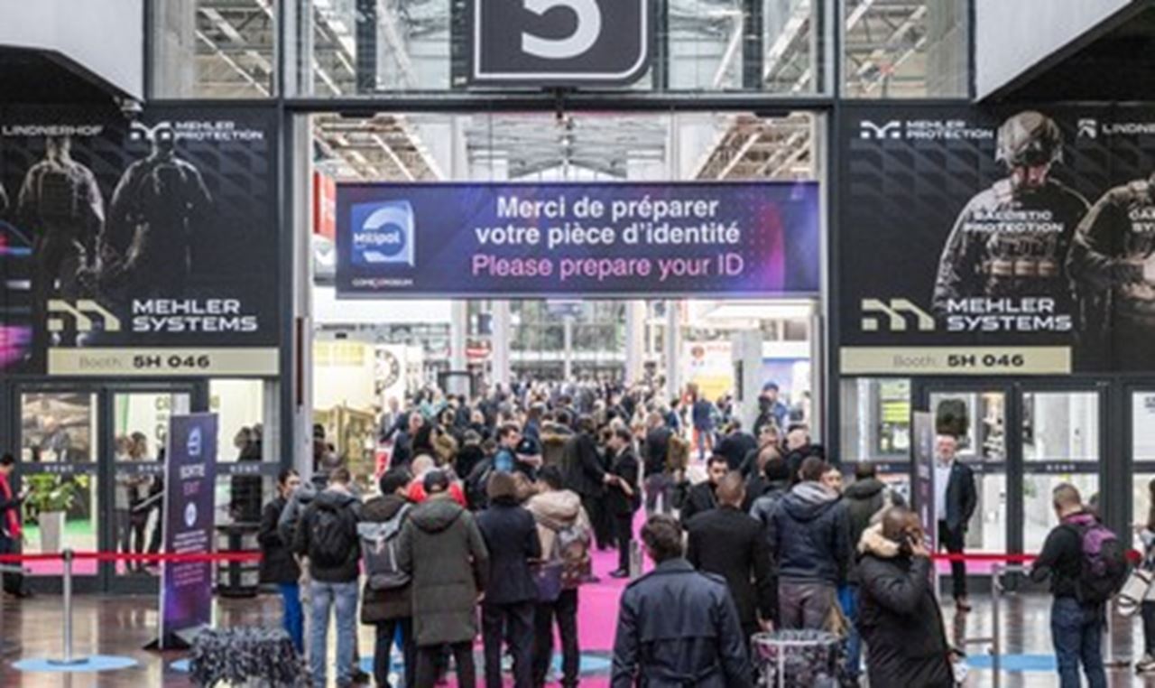 View of a crowd entering Milipol paris show under a large banner reading "Please prepare your ID" above the entrance to Hall 5. Event advertisements are visible on both sides.