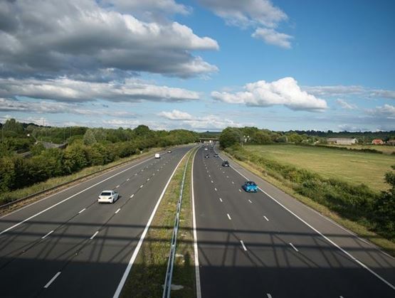 Autoroute à plusieurs voies avec une circulation fluide, dans un paysage rural sous un ciel partiellement nuageux.