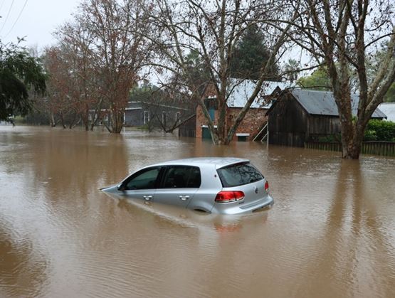 A grey car is in a middle of a flooded street
