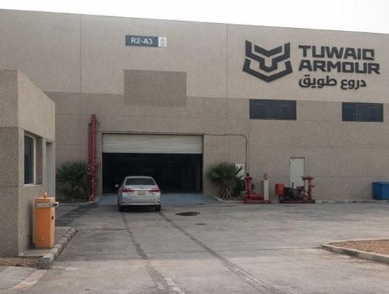 Facade of an industrial building displaying the “TUWAII ARMOUR” sign in English and Arabic, with an open warehouse door and a car parked in front of the entrance.