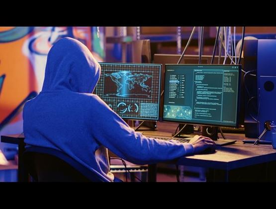 Personne en sweat à capuche devant plusieurs écrans affichant une carte du monde et du code informatique dans un contexte de cyberattaque