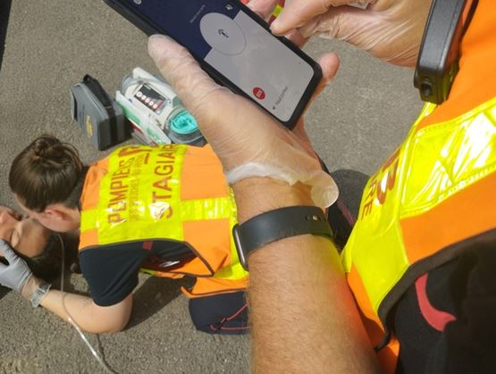Secouriste utilisant un smartphone pendant une intervention d’urgence, avec une victime au sol et du matériel médical à proximité.
