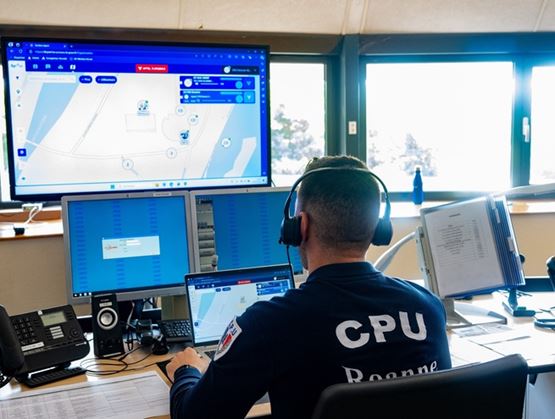 Opérateur de centre de supervision devant plusieurs écrans affichant une carte et des interfaces de suivi.