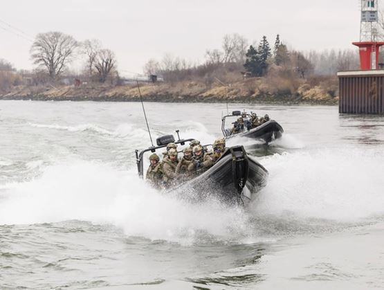 Deux embarcations rapides transportant des soldats en tenue tactique naviguent à grande vitesse sur une rivière, soulevant des gerbes d’eau lors d’une opération militaire.