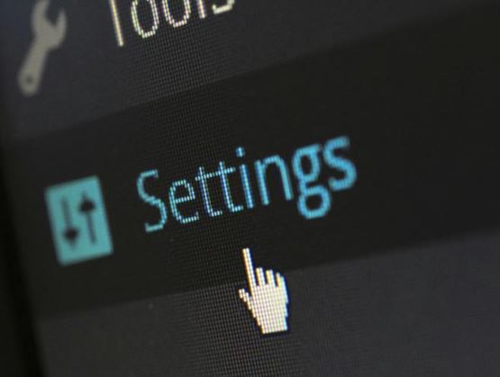 Gros plan sur une interface numérique affichant le menu “Settings” avec un curseur en forme de main pointant vers l’option de configuration.