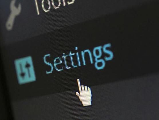 Close-up of a digital interface displaying the “Settings” menu with a hand-shaped cursor pointing to the configuration option.