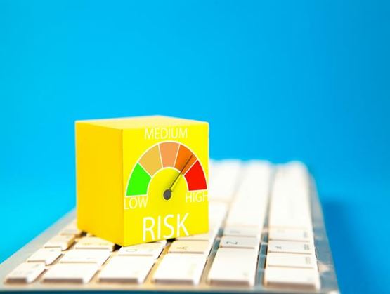 Cube jaune posé sur un clavier d’ordinateur avec une jauge de risque allant de faible à élevé, illustrant la gestion des risques numériques.