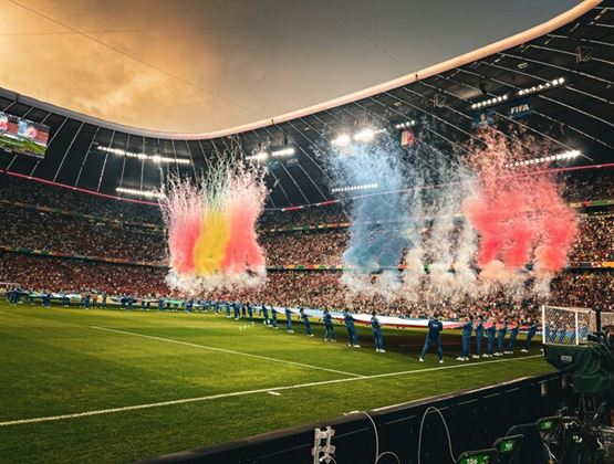 Opening ceremony in a packed football stadium, with coloured smoke effects and spectators in the background.