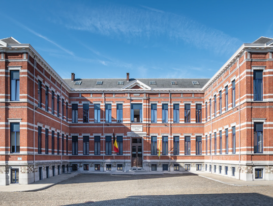 Historic red-brick FN Browning Group building with Belgian flags in front of the main entrance.