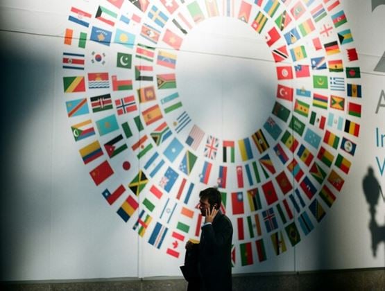 Man speaking on a phone in front of a circular display made up of international flags.