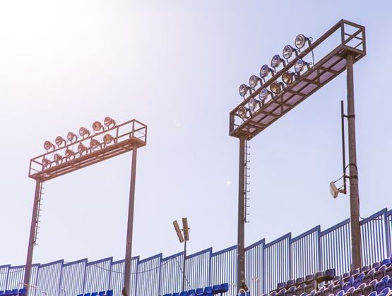 Stadium floodlights and seating under a bright sky, suggesting outdoor infrastructure exposed to strong heat.