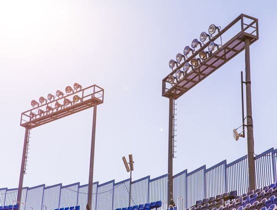 Stadium floodlights and seating under a bright sky, suggesting outdoor infrastructure exposed to strong heat.