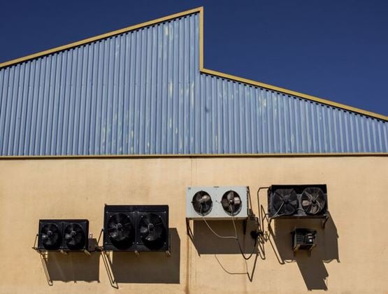 Air-conditioning units installed on the exterior wall of an industrial building under a clear blue sky.