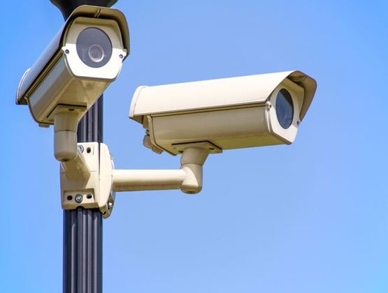 Deux caméras de surveillance extérieures fixées sur un poteau sous un ciel bleu dégagé.