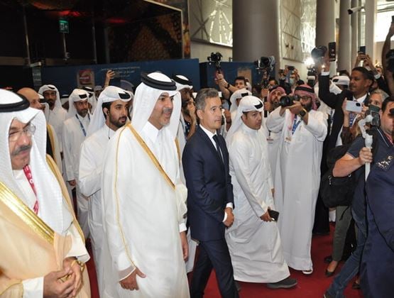 Officials and delegates walking through a security exhibition surrounded by photographers and media.