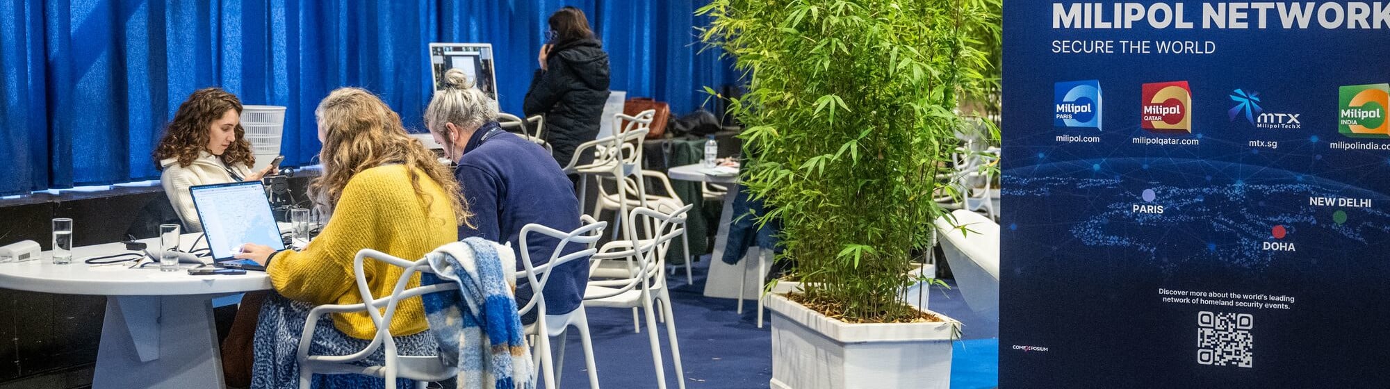 Des journalistes travaillent sur leurs ordinateurs portables dans l’espace presse du salon Milipol, à côté d’un kakémono présentant les événements du réseau Milipol.