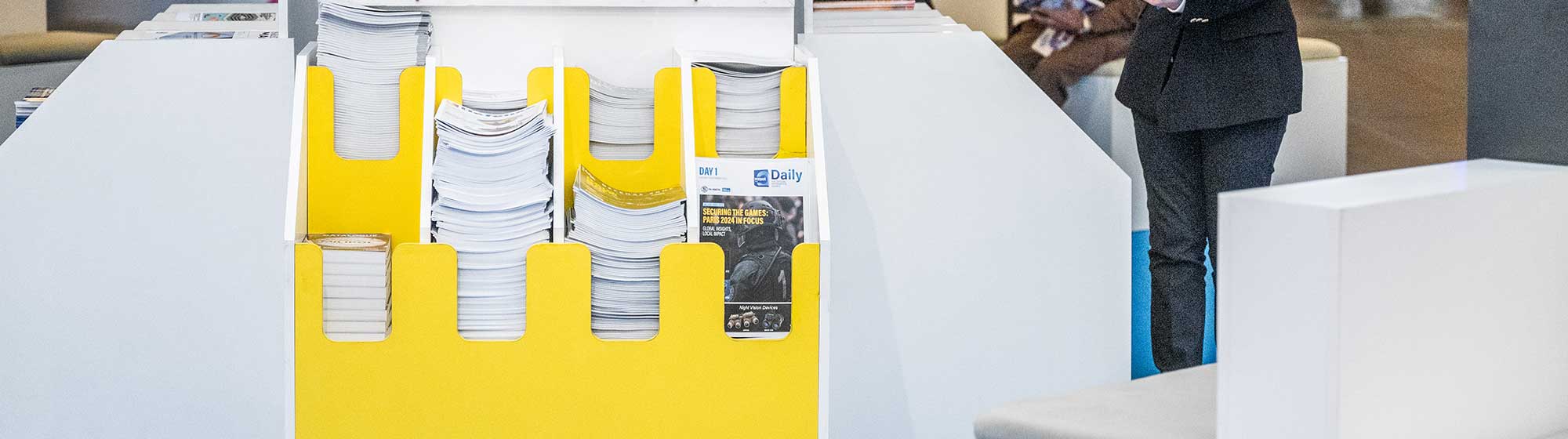 A newspaper stand indoor at Milipol Paris event, offering free papers to attendees.