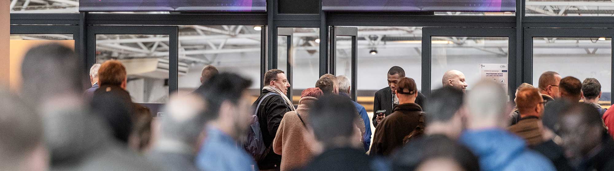 Crowded Milipol entrance security checkpoint with signs instructing passengers to prepare their IDs.