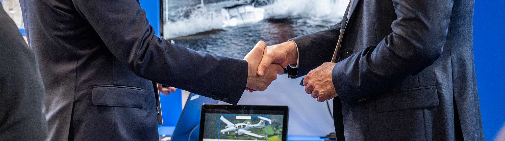 Deux hommes se serrant la main face à un ordinateur projetant un logiciel de simulation