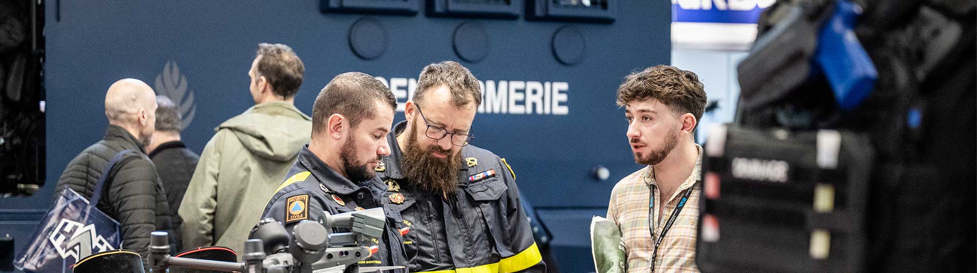 Deux hommes de la sécurité civile en uniformes militaires se tiennent autour d'une table auprès d’un visiteur 