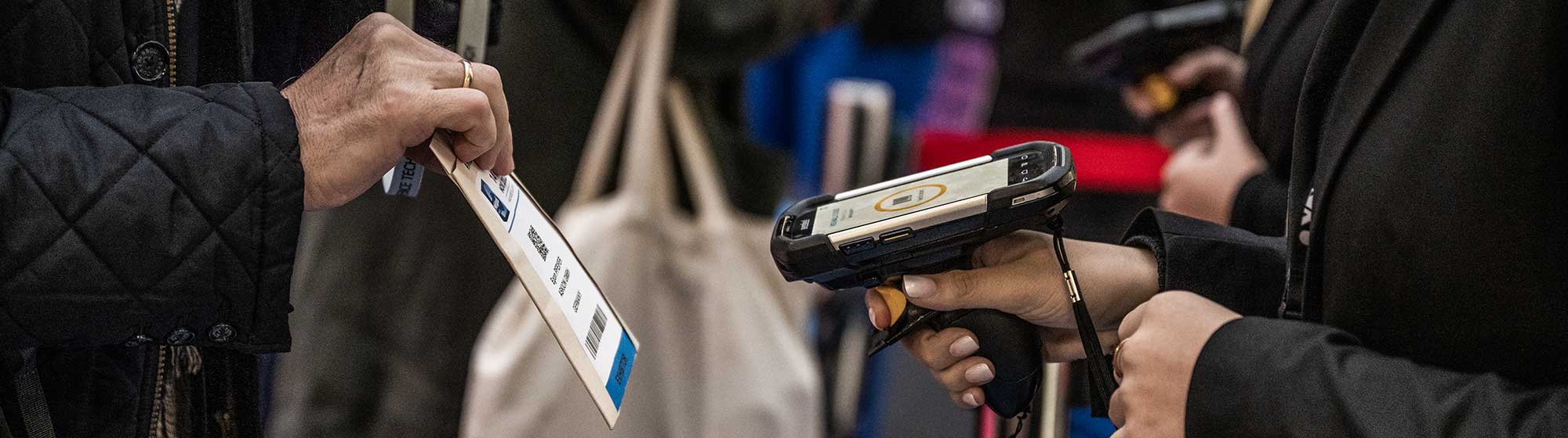 Une personne présente son badge à une autre personne qui le scanne à l'aide d'un appareil portable. L'image montre l'entrée de l'événement Milipol Paris.
