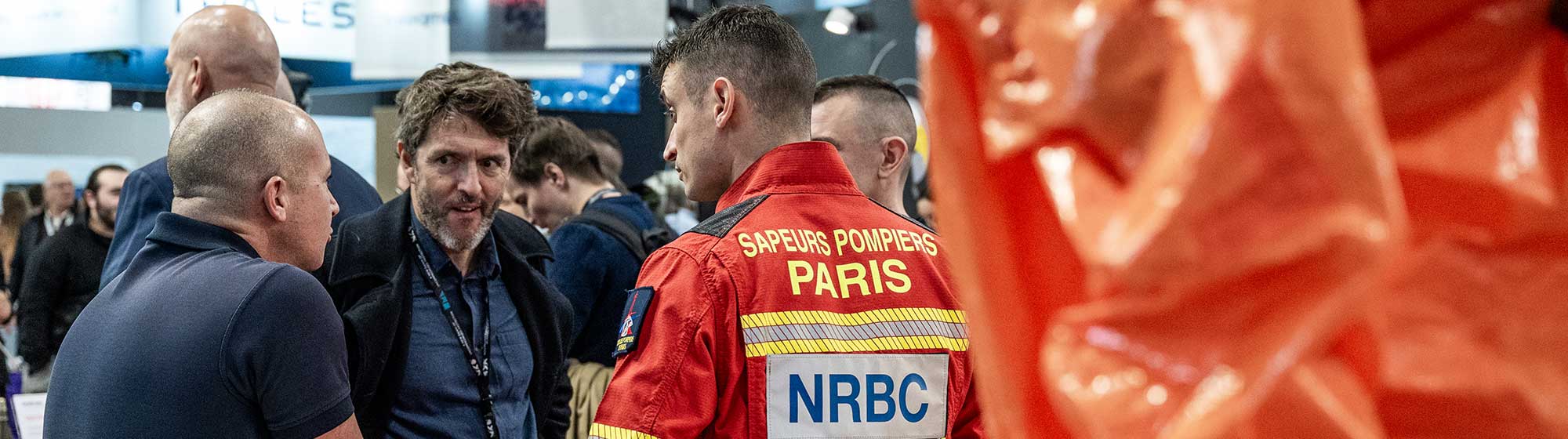 Discussion sur le stand de la BSPP entre un visiteur et deux sapeurs-pompiers en uniforme