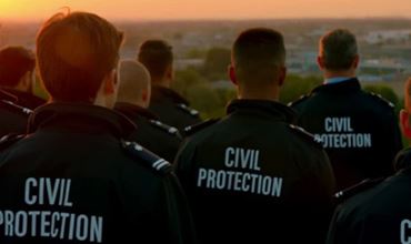 Group of Civil Protection members watching the sunset, with their jackets displaying the "CIVIL PROTECTION" inscription.