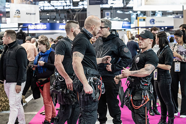 RAID police officers, some equipped with climbing gear, surrounded by exhibition stands at Milipol Paris