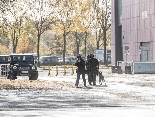 Policiers du RAID avec un chien près d'un bâtiment et d'un véhicule