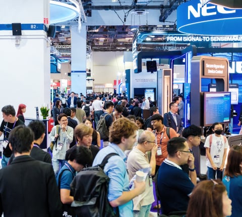 Une allée pleine de visiteurs avec des stands exposants sur le côté durant MTX Milipol TechX