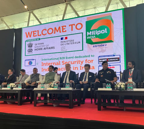 8 men seated on stage in the conference room at the Milipol India event, some of them are in uniform