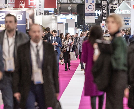 Busy Milipol's aisle with various booths and a crowd of attendees walking on a pink carpet. The faces of individuals are obscured for privacy.