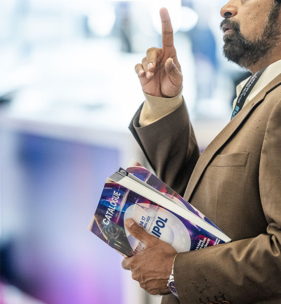 Homme pointant l'index vers le haut un exemplaire du catalogue milipol à la main gauche
