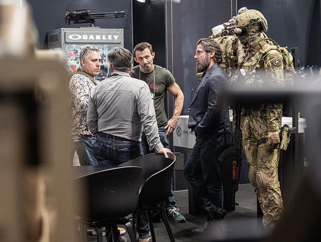 3 men discussing on the Oakley stand surrounded by military uniforms