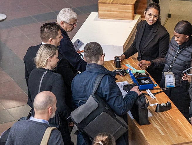 Un groupe de personnes est rassemblé autour d'un bureau d'inscription et reçoit des documents et des badges de la part du personnel