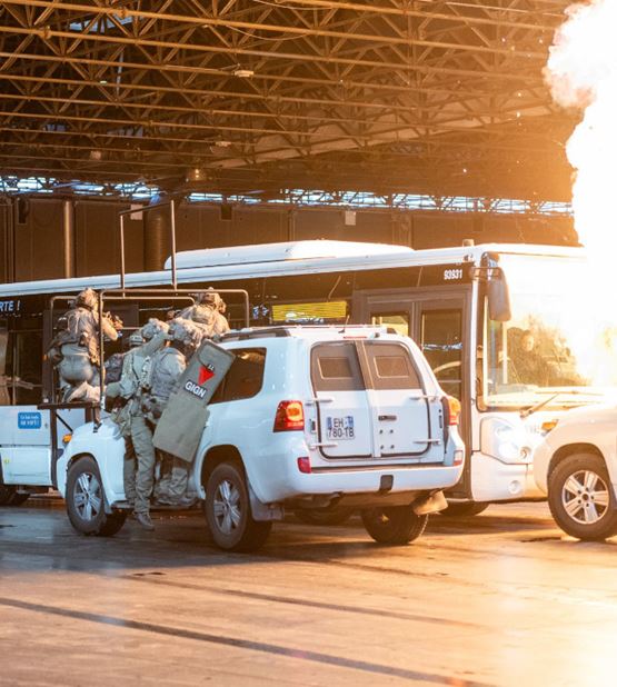 Simulation d’intervention du GIGN pendant Milipol Paris, avec des agents en tenue tactique montant à bord d’un bus à l’aide d’un véhicule d’assaut, sous une explosion contrôlée