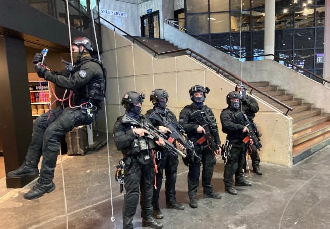 A group of armed police officers from the intervention brigade (BI/DOPC) in black uniforms going down from the roof with ropes.